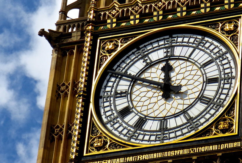 A close-up of the Big Ben clock tower face in London with a blue sky and puffy clouds in the background