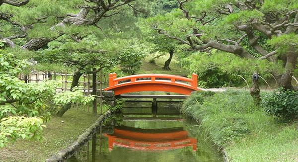 A footbridge over a pond in lush wooded area of Japan