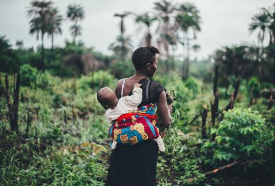 A woman works in a field while carrying her baby on her back.