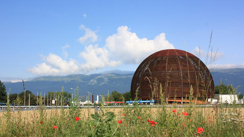 A large spherical wooden structure set against a backdrop of mountains and blue sky with scattered clouds