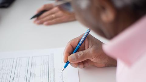 A close-up of a person sitting at a desk and signing a document with a blue pen
