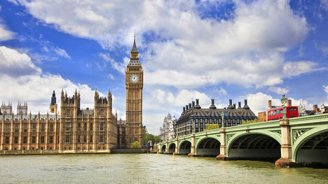 Palace of Westminster and Big Ben alongside Westminster Bridge with a red double-decker bus crossing the River Thames under a bright blue sky