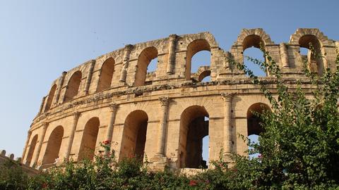 An ancient Roman amphitheater in Tunis with large stone arches and a weathered facade under clear blue sky