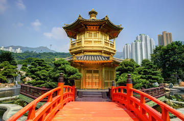 Gold Pavilion of Perfection in Hong Kong situated in a garden with a bright red arched bridge leading to its entrance and high-rise buildings in the background
