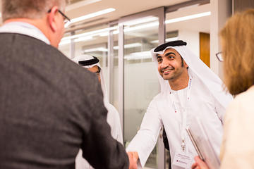 A man in traditional Middle Eastern attire shaking hands with a man in a suit in an office setting