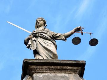 Statue of Lady Justice holding a sword in her right hand and balanced scales in her left hand against a clear blue sky