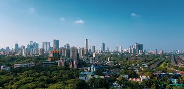 Mumbai skyline featuring numerous high-rise buildings under a clear blue sky with dense green trees in the foreground