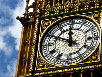 Close-up view of Big Ben's clock face indicating the time as 11:50, set against a partly cloudy blue sky background