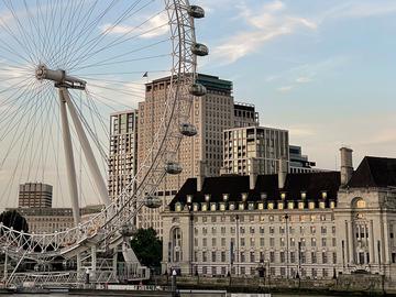 London Eye, a large ferris wheel on the South Bank of the River Thames, with surrounding buildings under a clear blue sky