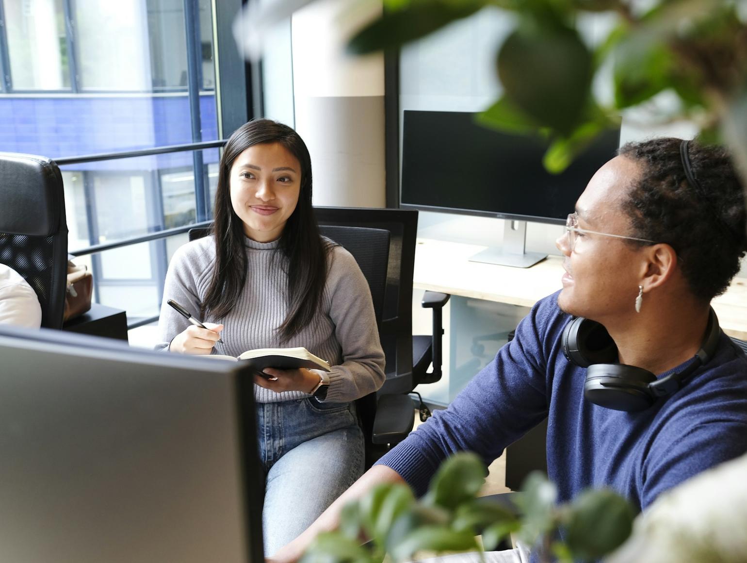 Two coworkers engaged in a discussion in an office setting with computers 