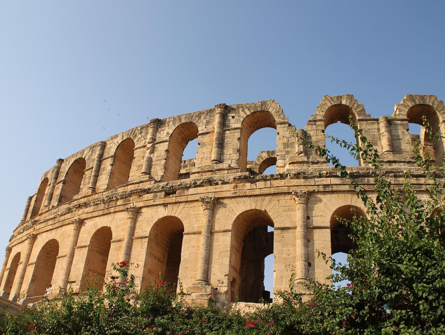 An ancient Roman amphitheater in Tunis with large stone arches and a weathered facade under clear blue sky
