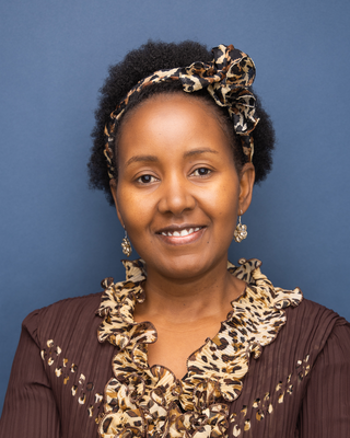 A smiling woman with dark brown eyes and short curly hair wearing a brown blouse with leopard print ruffles and matching headband against a blue background